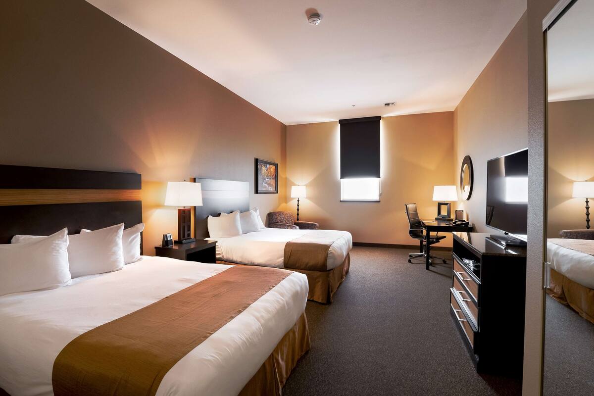 Une chambre d’hôtel avec deux lits, un bureau, une chaise, une télévision et une grande fenêtre.