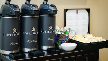 Tres dispensadores de agua negros de hotel con la etiqueta "HOTEL MAISON Descafeinado", un cuenco de aperitivos y un tablero de menú.