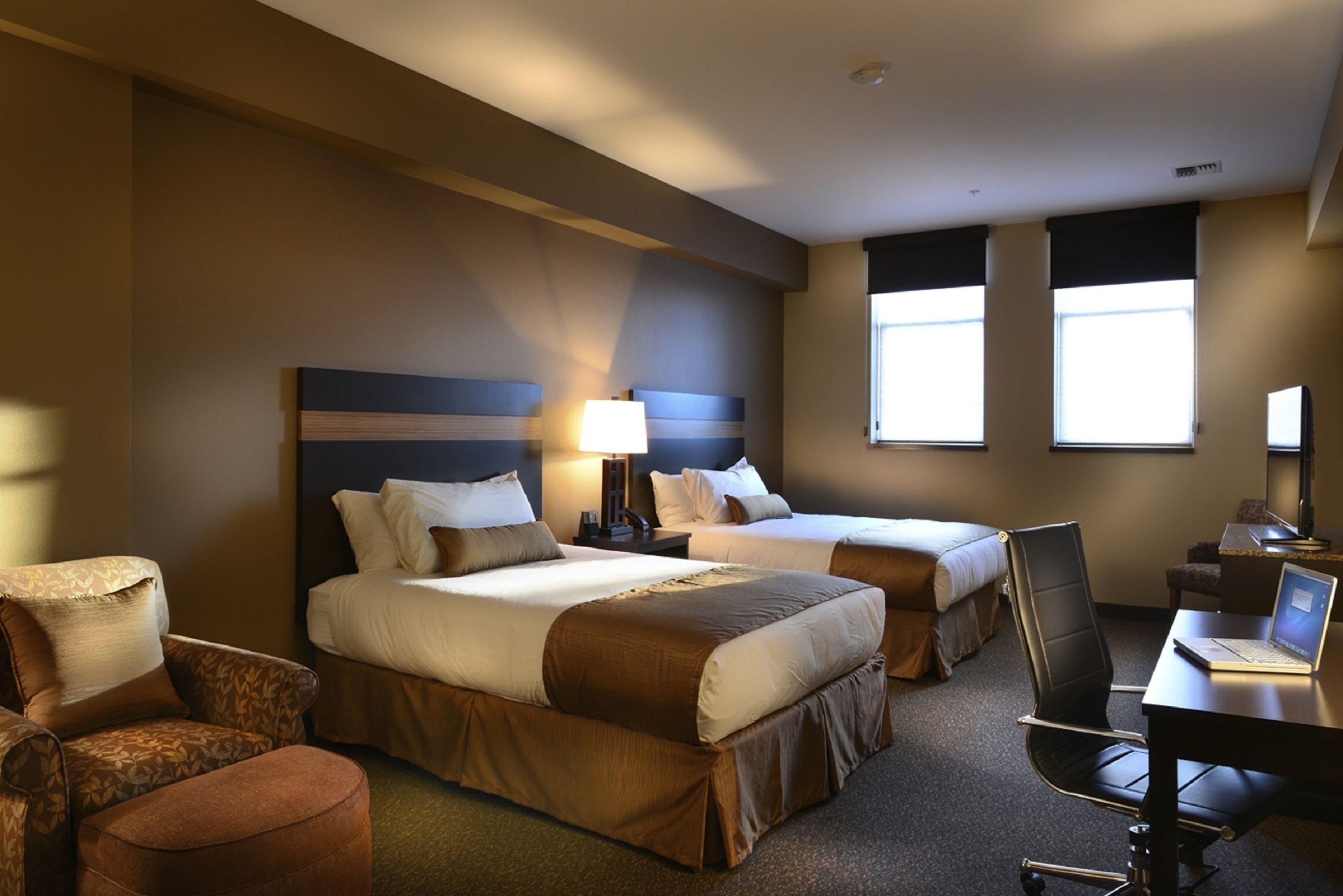 A hotel room with two beds, a desk, a chair, and a TV.