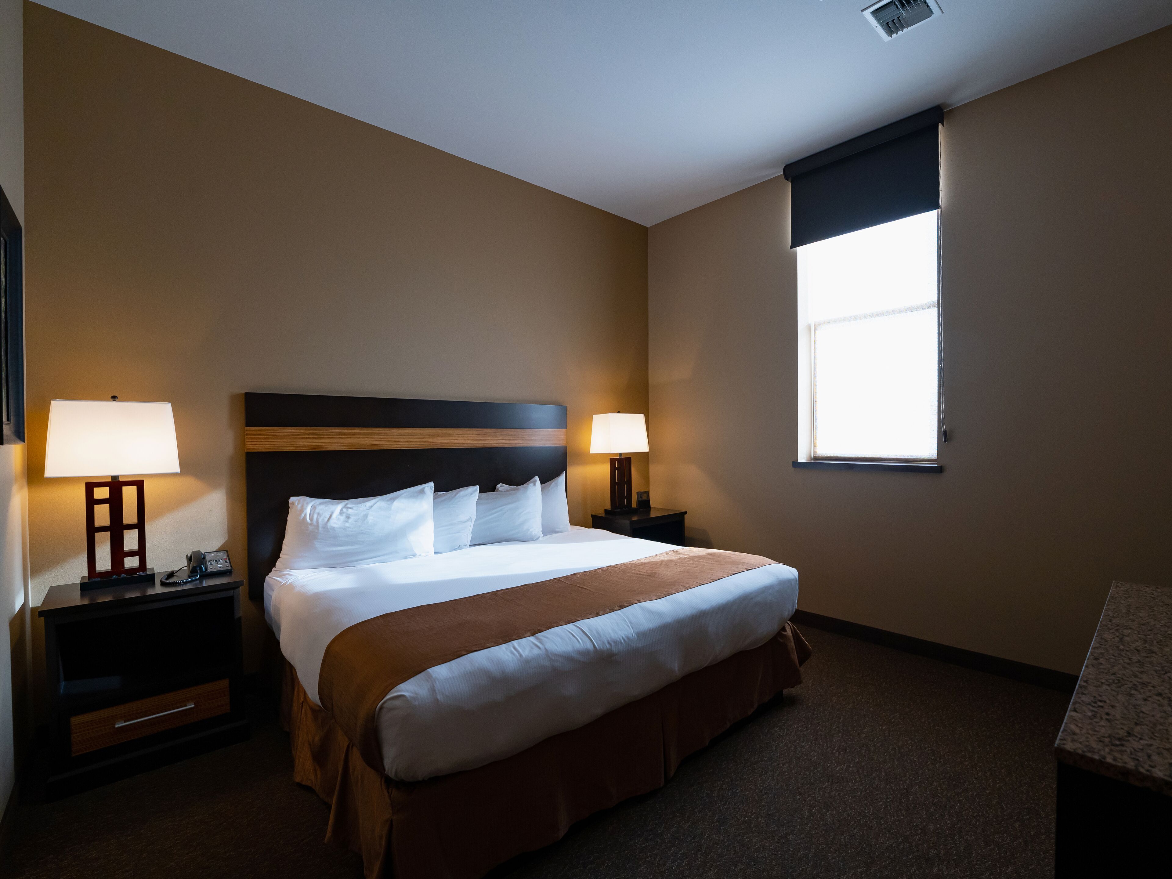 Een hotelkamer met een groot bed, twee nachtkastjes met lampen, een raam en een vloerbedekking.