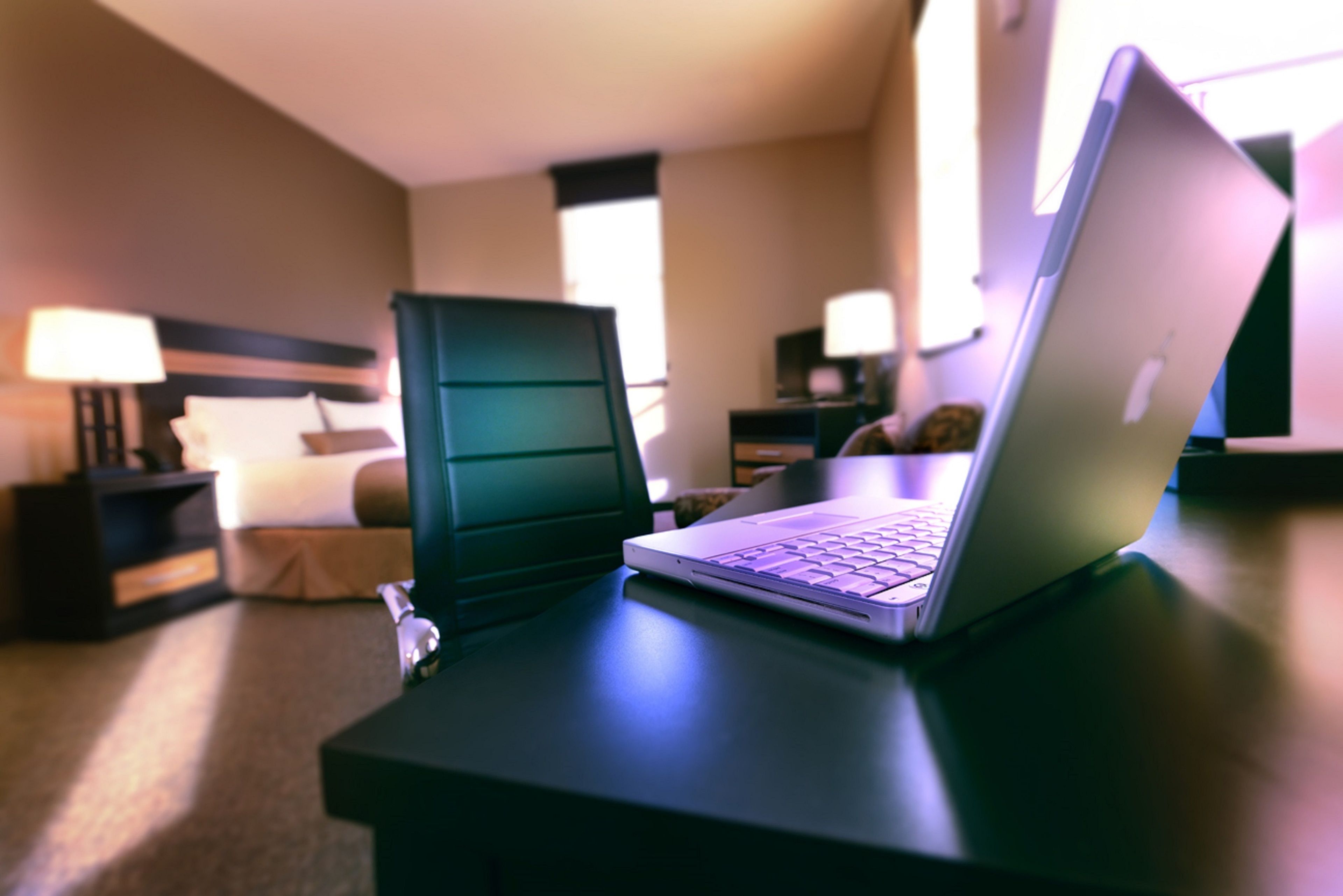 Una habitación de hotel con una cama, un escritorio con una computadora portátil y una mesita de noche con una lámpara.