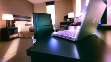 Una habitación de hotel con una cama, un escritorio con una computadora portátil y una mesita de noche con una lámpara.
