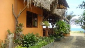 A building with a thatched roof, surrounded by lush greenery and a gravel path leading to the beach. - Hotel Hosteria Nantu (Puerto Lopez)