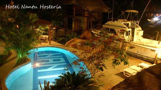 A swimming pool with a tropical setting, surrounded by plants and a boat docked nearby. - Hotel Hosteria Nantu (Puerto Lopez)