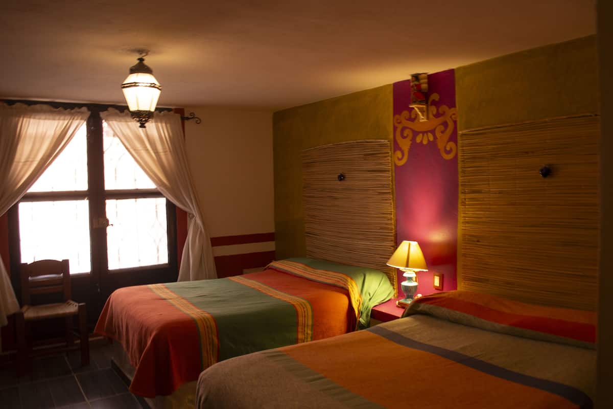 A hotel room with two beds, a chair, a window with curtains, and a lamp.