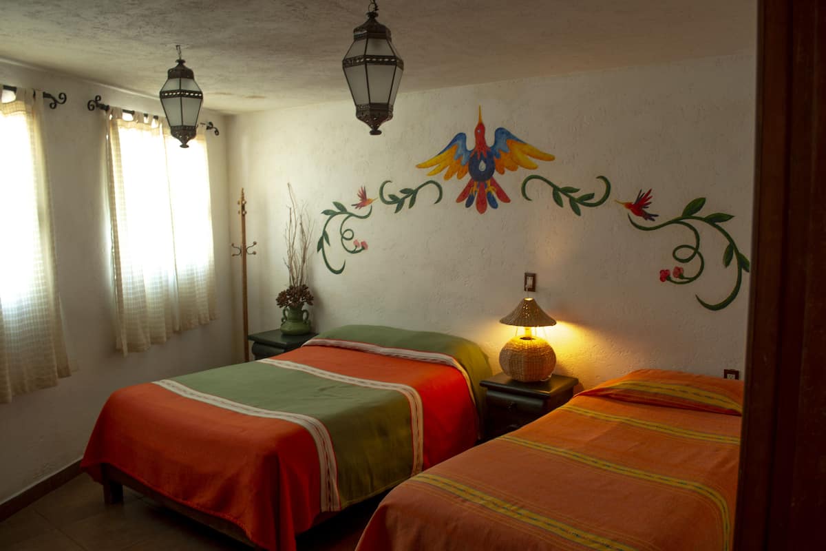 A room with two beds, a wall mural, and two hanging lanterns.