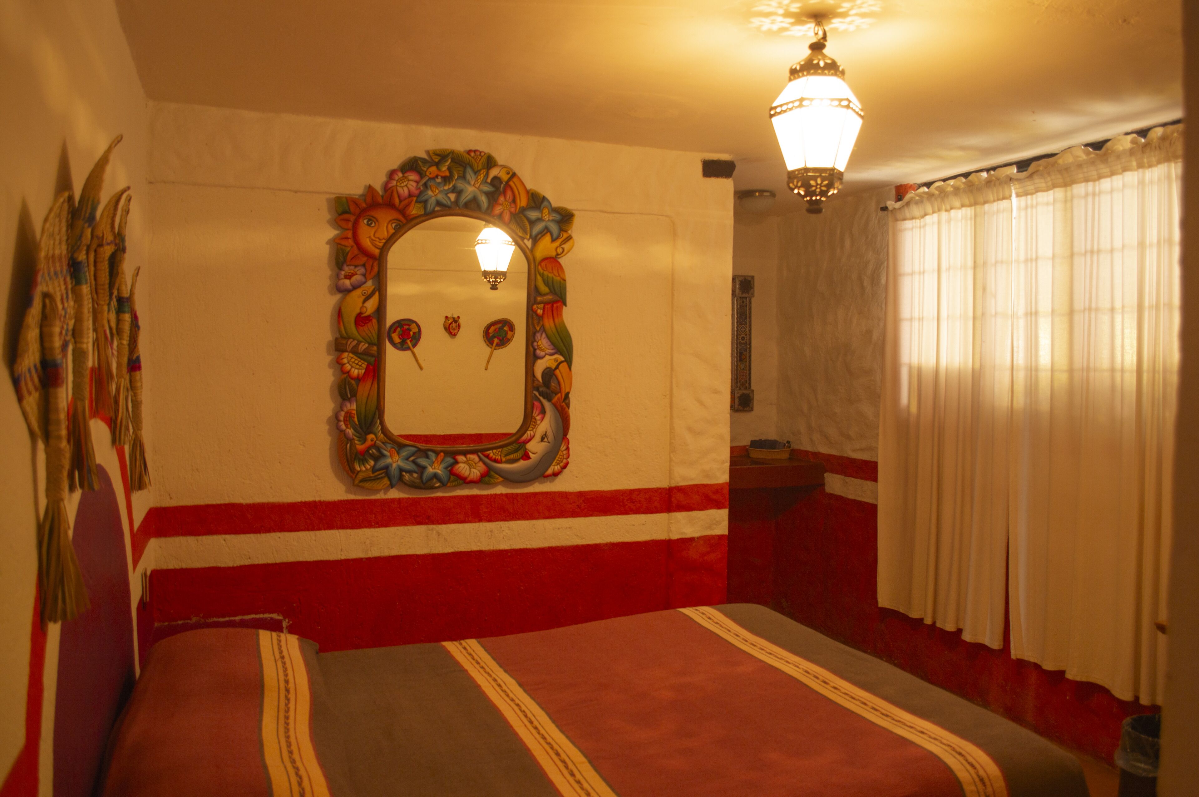 A room with a large mirror, a bed with striped bedding, a red and white wall, and a chandelier.