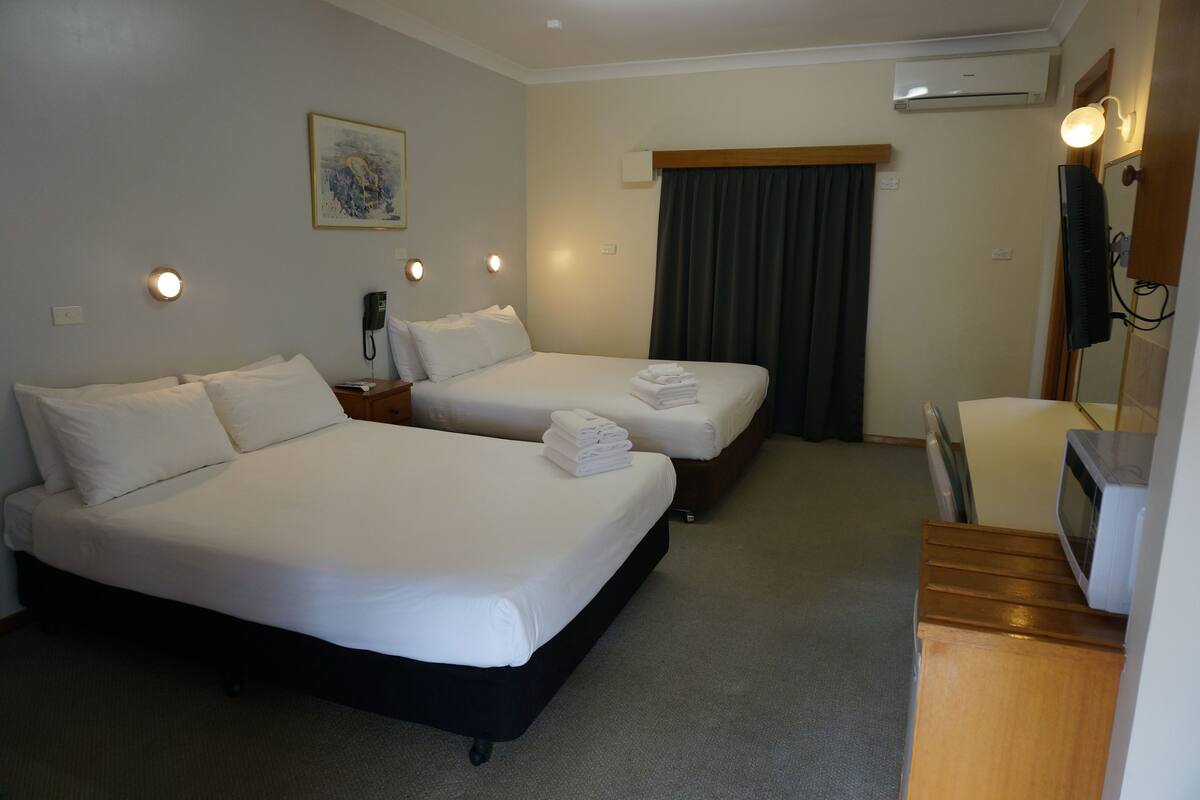 A hotel room with two beds, a desk, a chair, a TV, and an air conditioning unit.