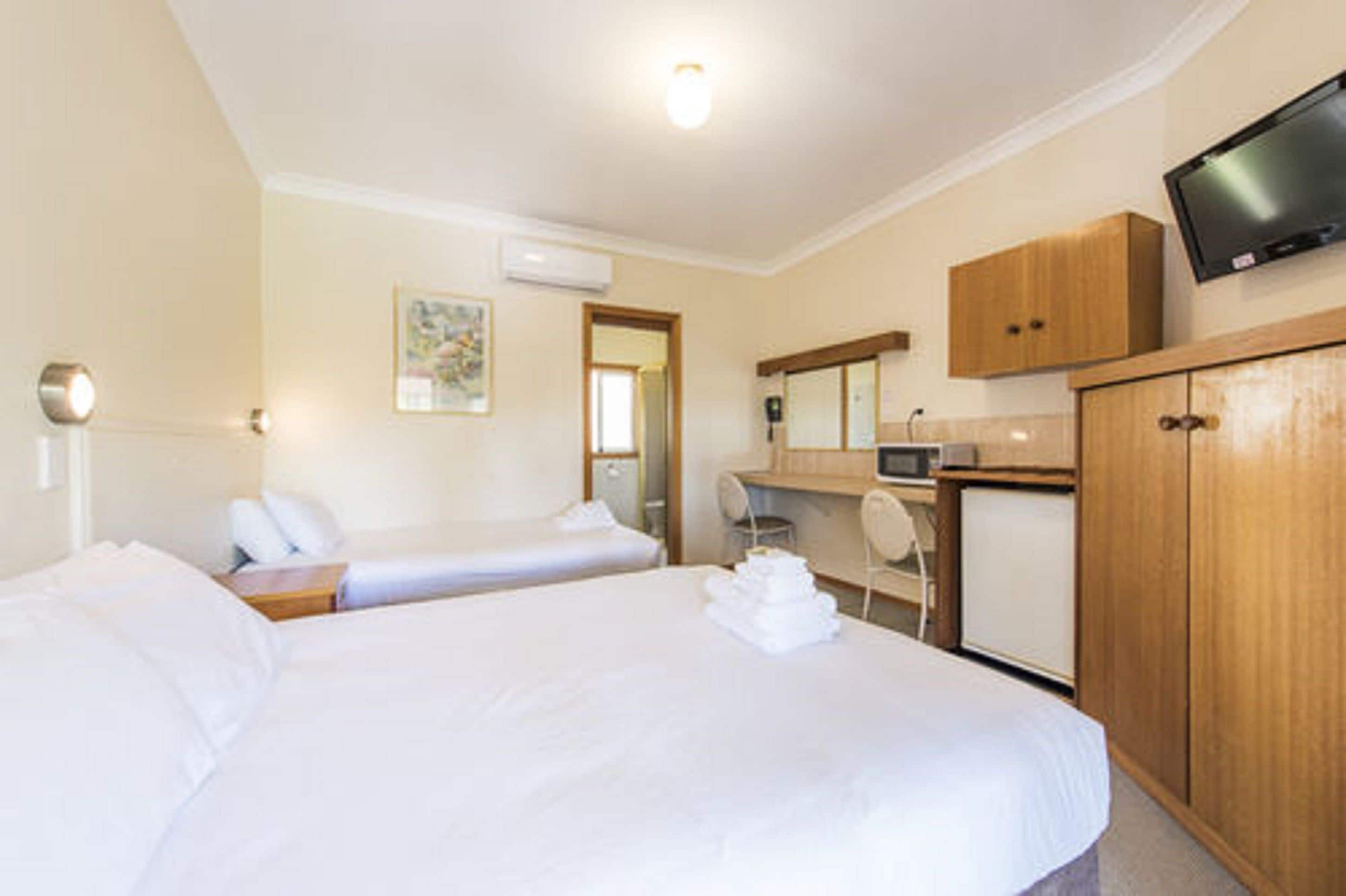 Habitación de hotel con dos camas, un escritorio, televisor y armario.