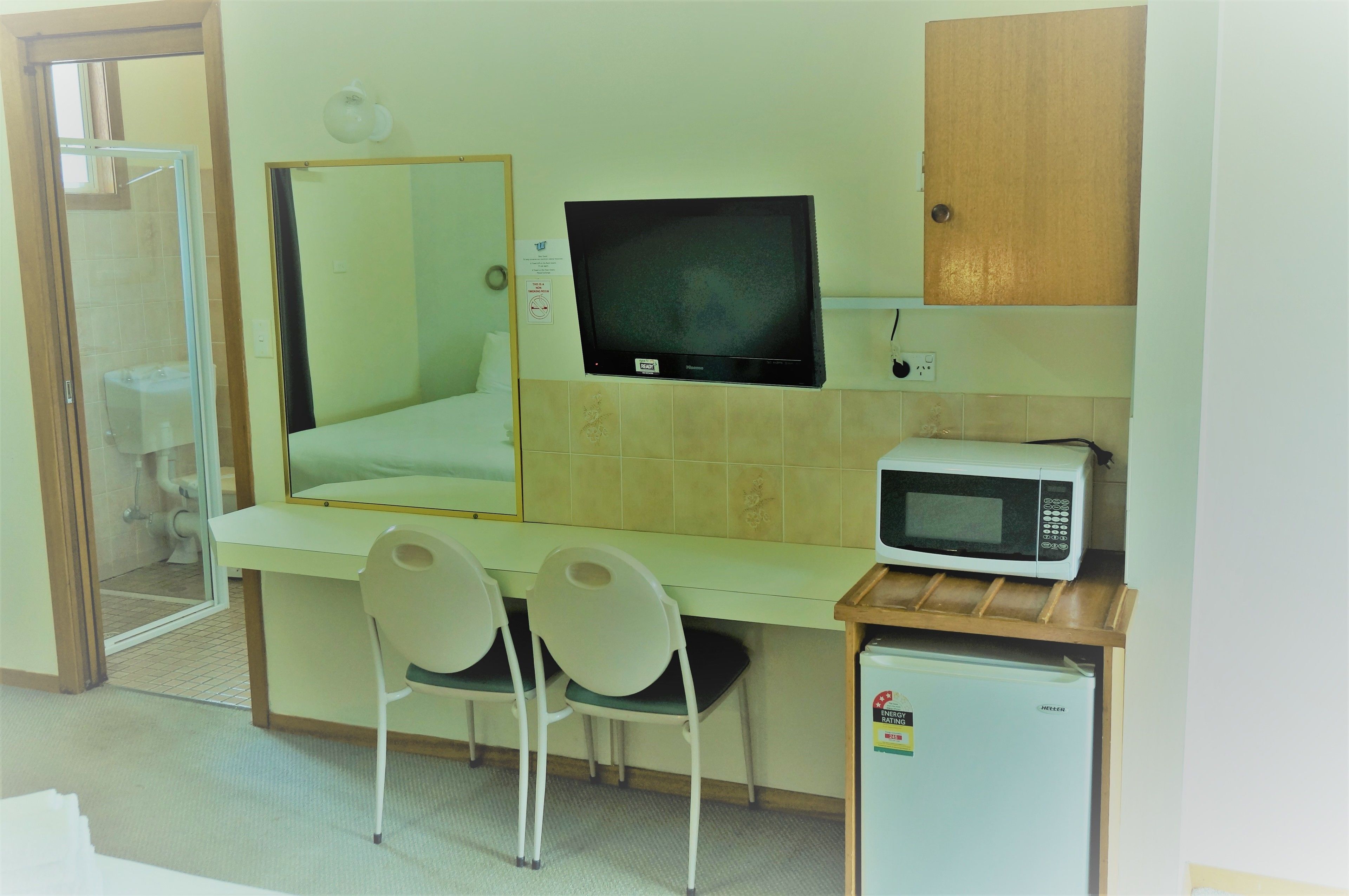 A small kitchenette with a microwave, a refrigerator, and a sink. There are two chairs and a mirror above the sink.