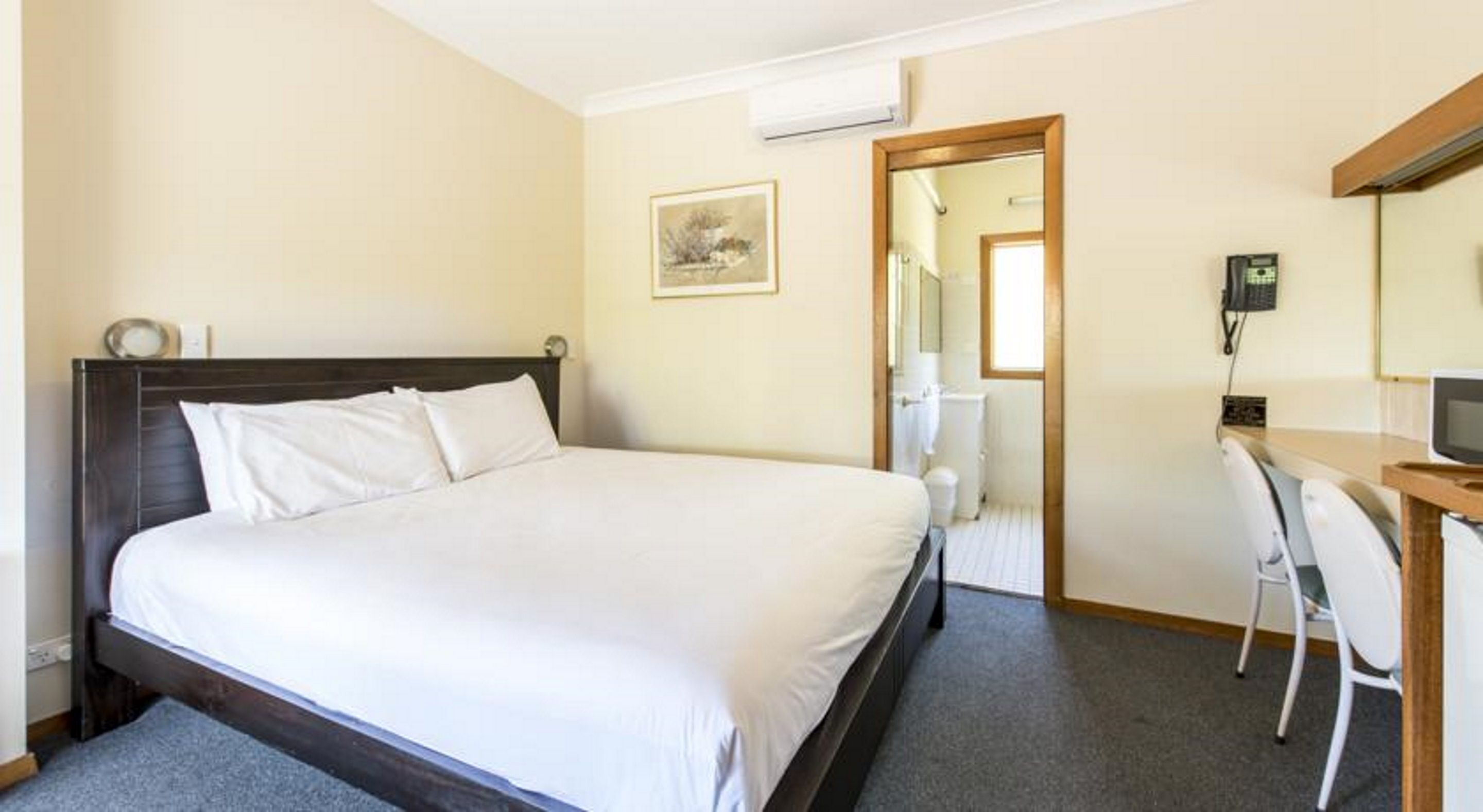 A hotel room with a single bed, a desk with a chair, a mirror, and a picture on the wall.