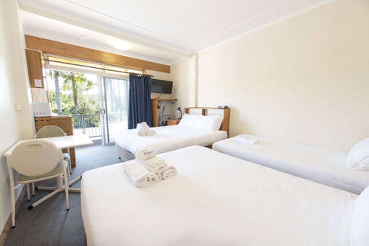A hotel room with two beds, a desk, a chair, and a TV.