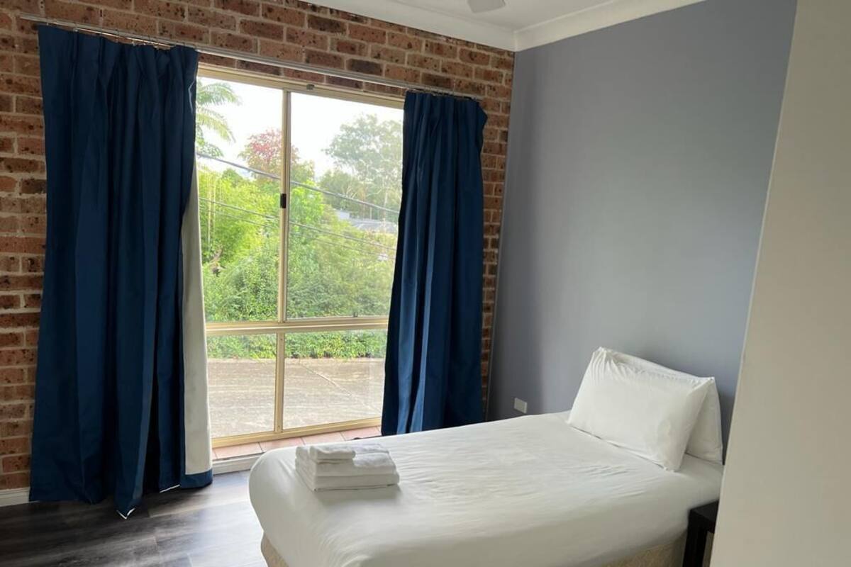 A bedroom with a bed, a window with curtains, and a view of greenery outside.