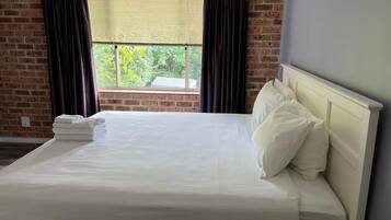 Cama bem arrumada com lençóis brancos em quarto com paredes de tijolo e janela com cortinas.