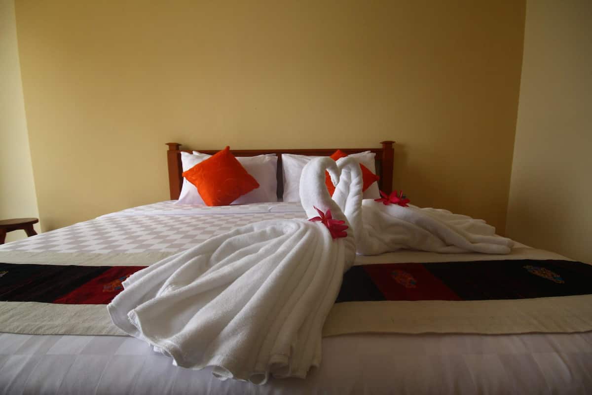 A neatly made bed with a checkered bedspread, white pillows, and a single orange pillow.