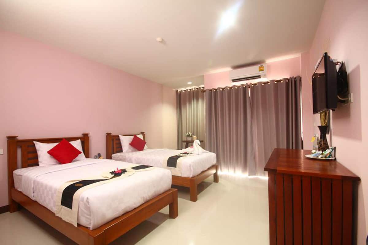 A hotel room with two beds, a wooden desk, and an air conditioning unit.