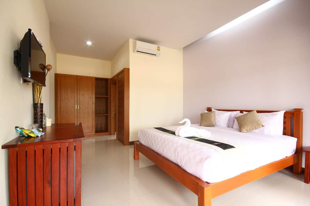 A hotel room with a wooden bed, a wooden desk, a mirror, and a wardrobe.