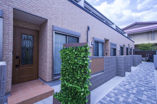 A brick building with a wooden door, large windows, and a tiled walkway.