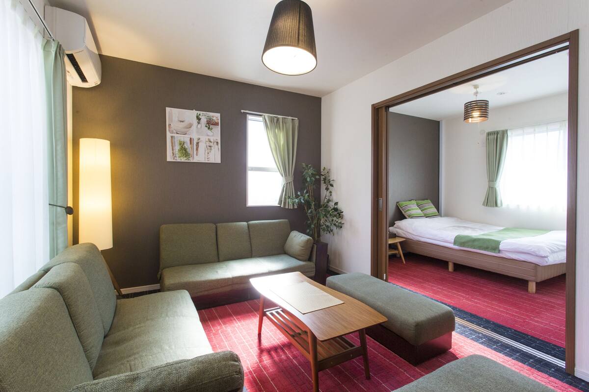 Moderni hotellihuone, jossa on sohva, pieni pöytä, sänky ja suuri peili.