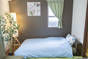 A bedroom with a bed, a bedside table, a lamp, a window with curtains, and a wall-mounted picture.