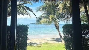 A covered outdoor area with a view of a beach and palm trees.