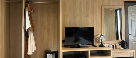 A hotel room with a wooden wardrobe, a television, a mini-fridge, a desk with a computer, and a bed.