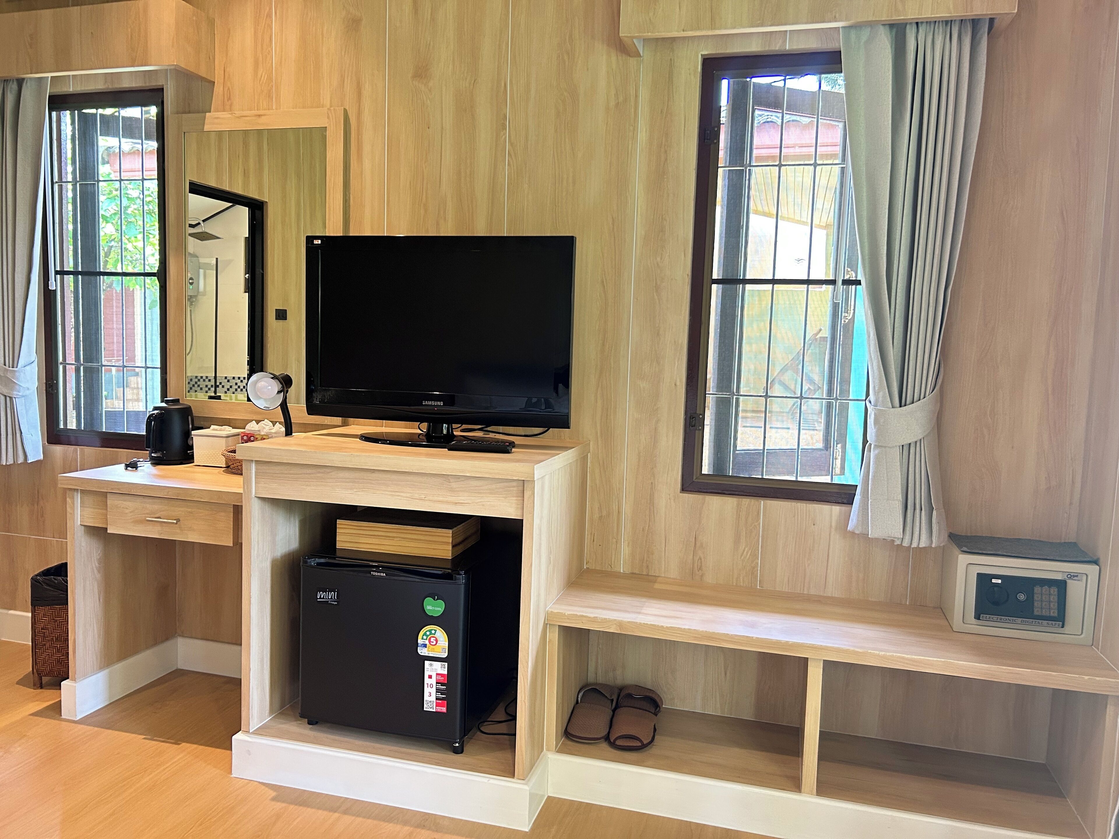 Camera d'albergo con una scrivania in legno, televisione, frigorifero e finestra con tende.