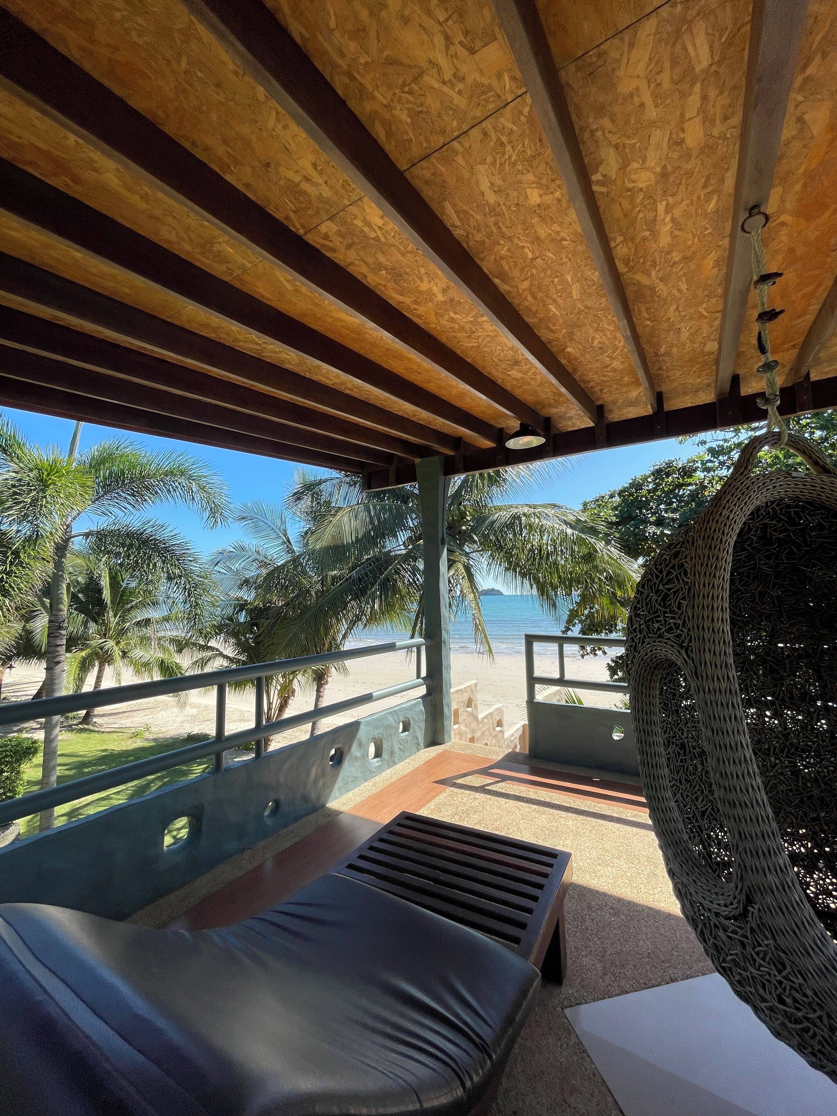 A covered outdoor seating area with a view of the beach and palm trees.