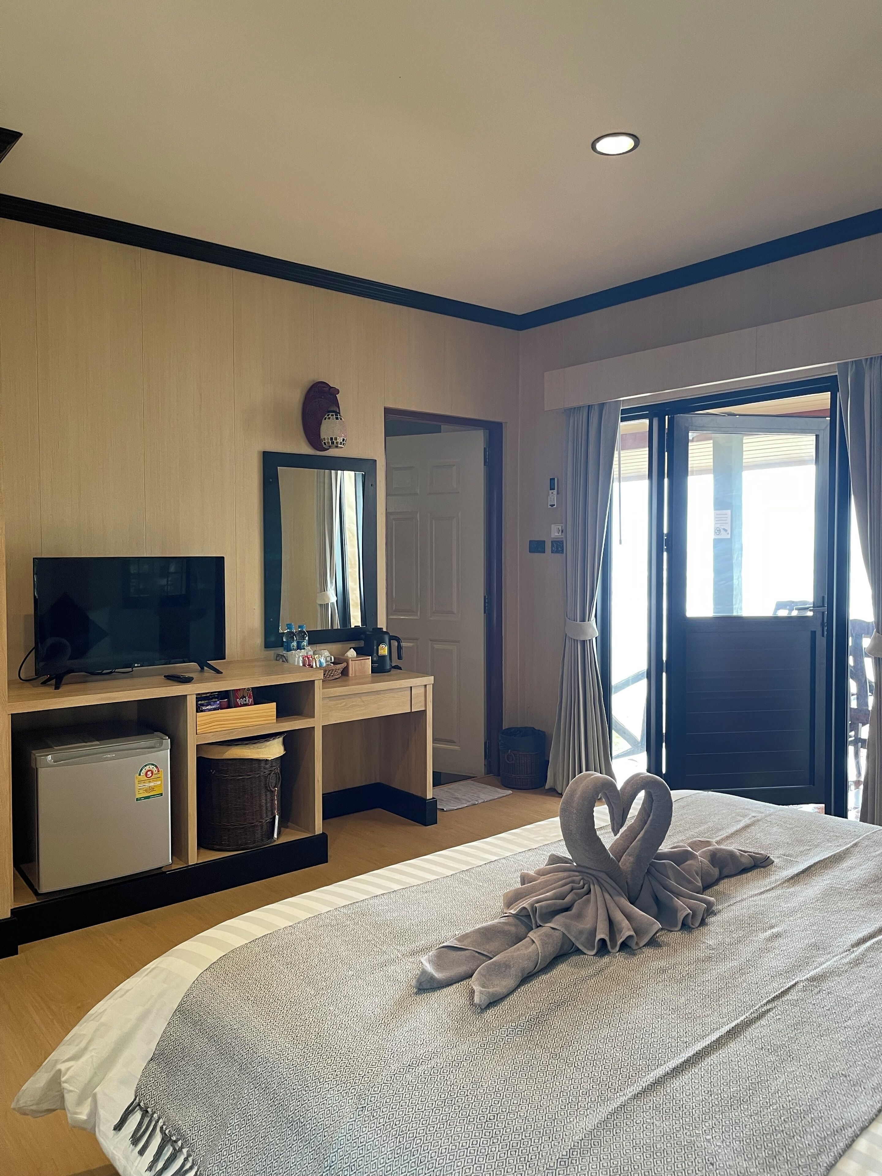Une chambre d’hôtel équipée d’un lit, d’une télévision, d’un bureau avec un ordinateur, d’un petit réfrigérateur et d’une fenêtre avec des rideaux.