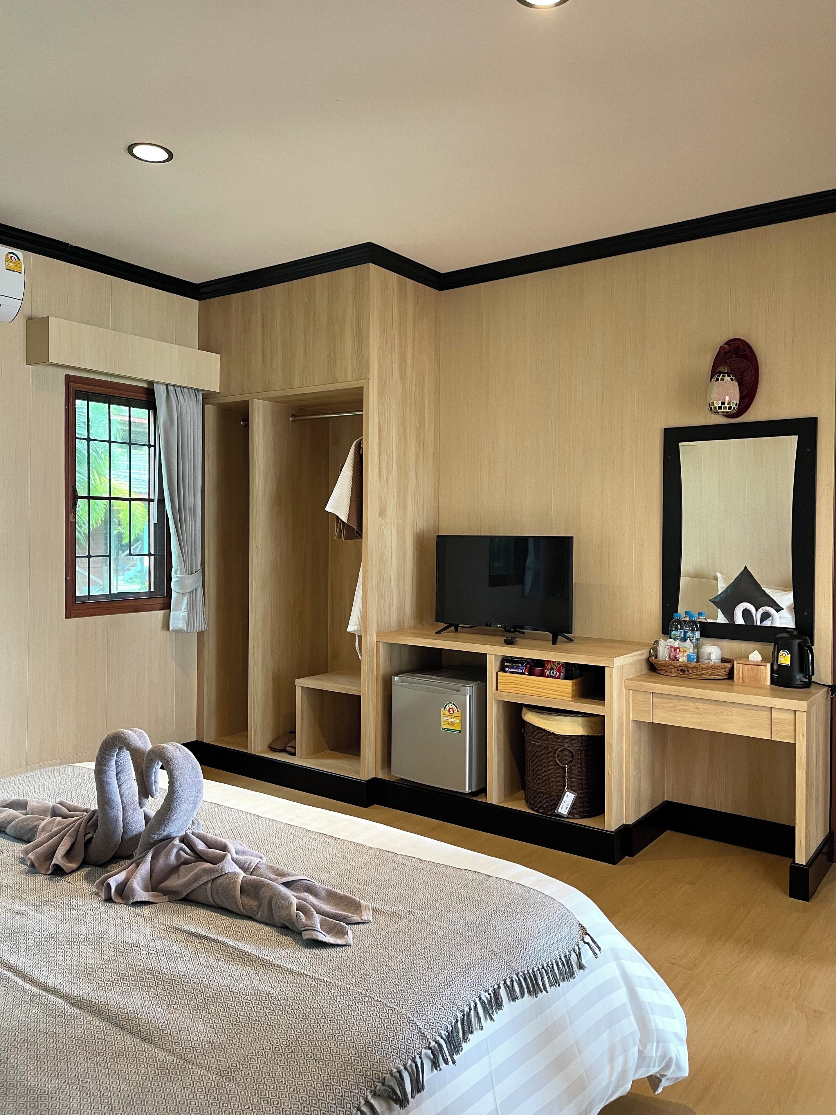 Habitación de hotel con cama, televisión, refrigerador pequeño, escritorio con espejo y ventana con cortinas.