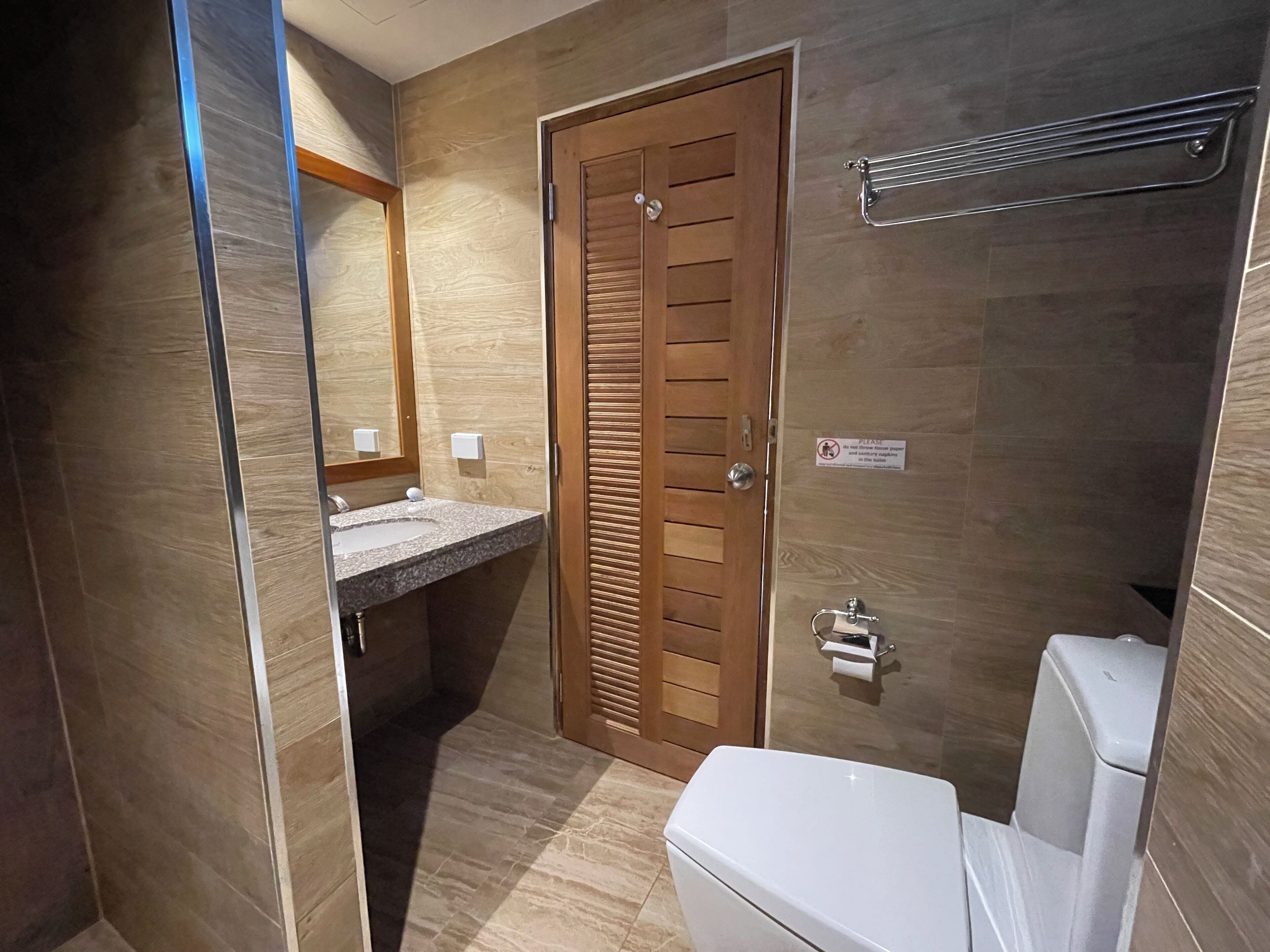 A bathroom with a wooden door, a sink with a mirror, and a toilet.