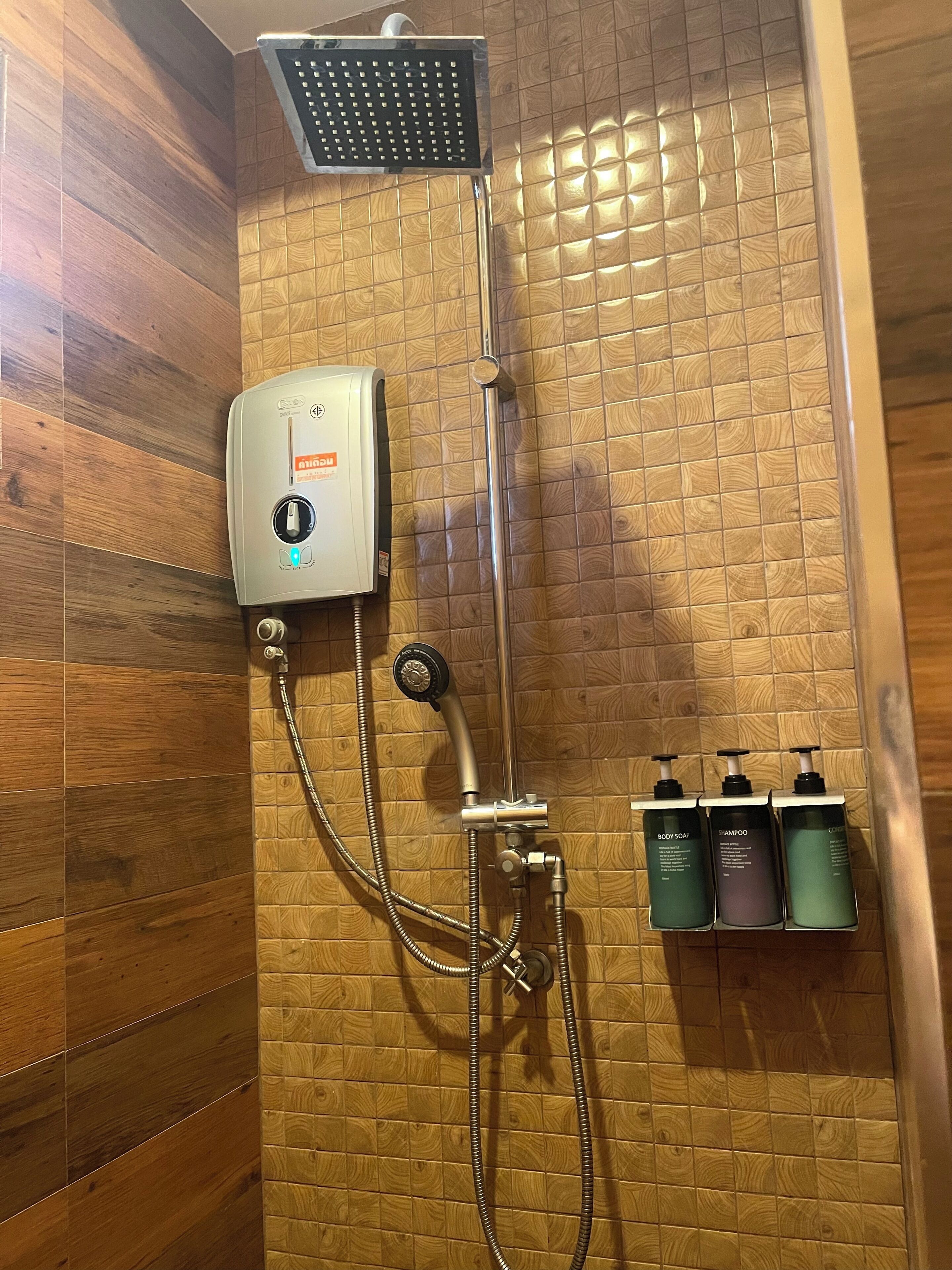 A shower with a handheld showerhead, a wall-mounted control panel, and a set of shampoo bottles.
