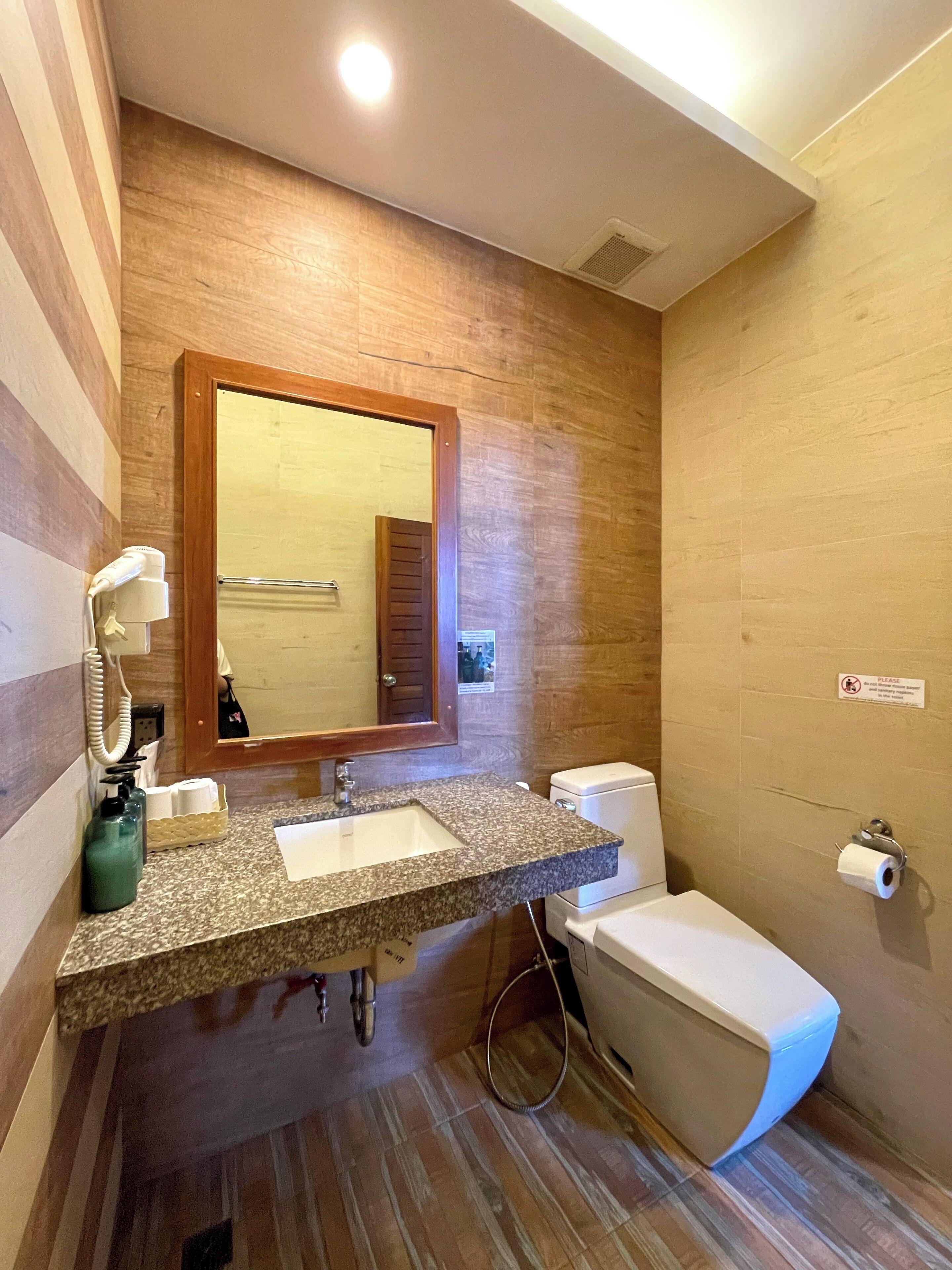 A bathroom with a granite countertop, a mirror, a toilet, and a shower area.