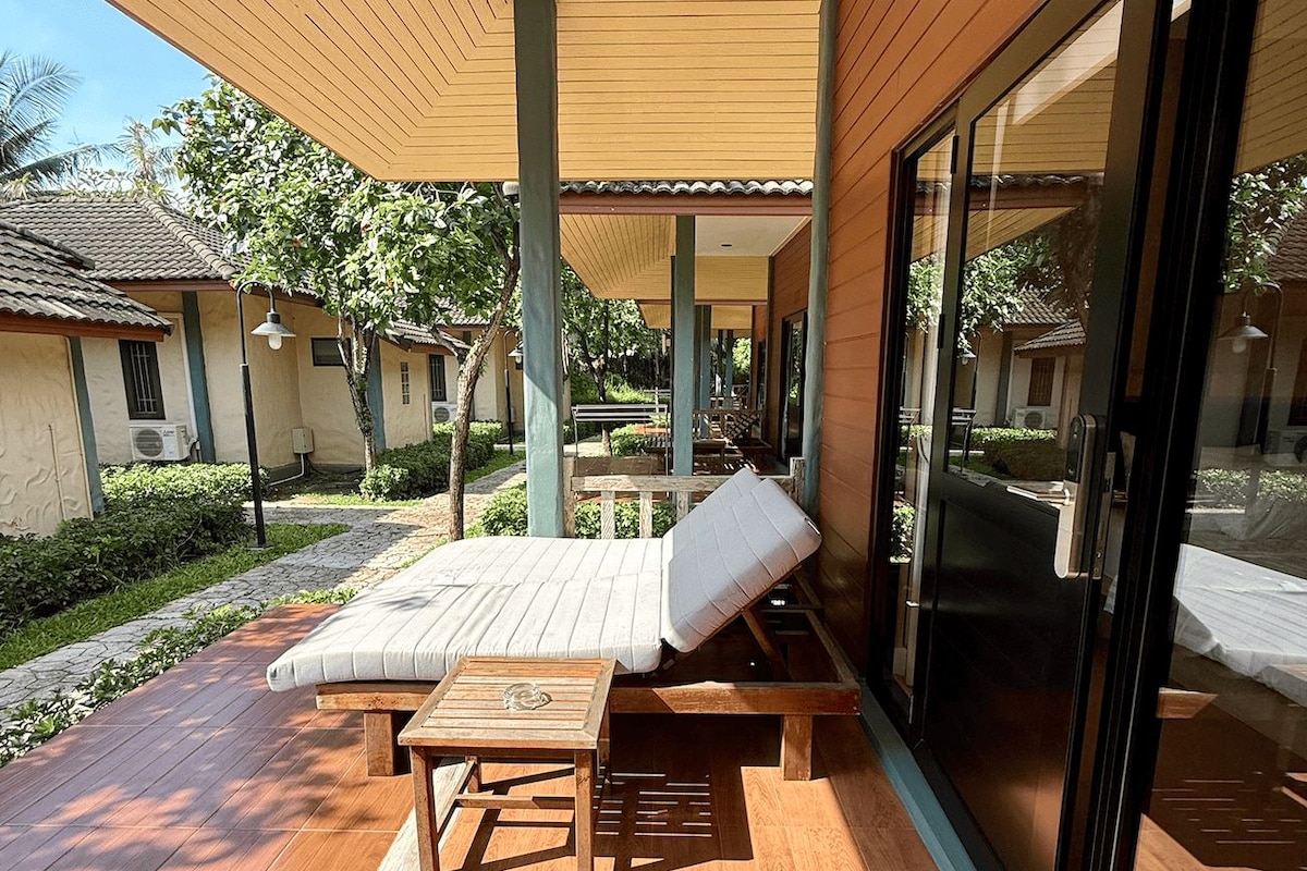 A covered outdoor seating area with a wooden deck, a lounge chair, and a table.