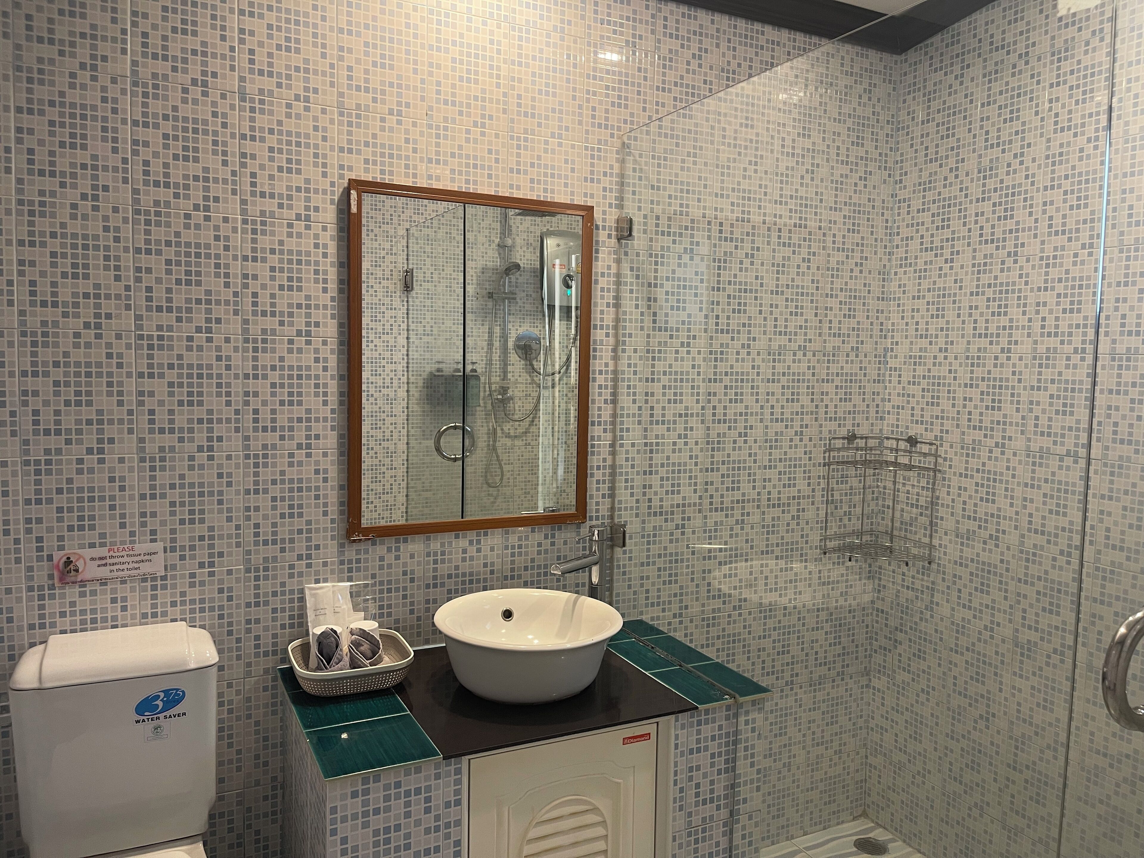 A bathroom with a tiled wall, a sink, a mirror, a shower, and a water-saving device.