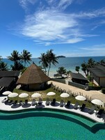 Un resort con piscina, sillas de descanso, sombrillas y vista al océano.