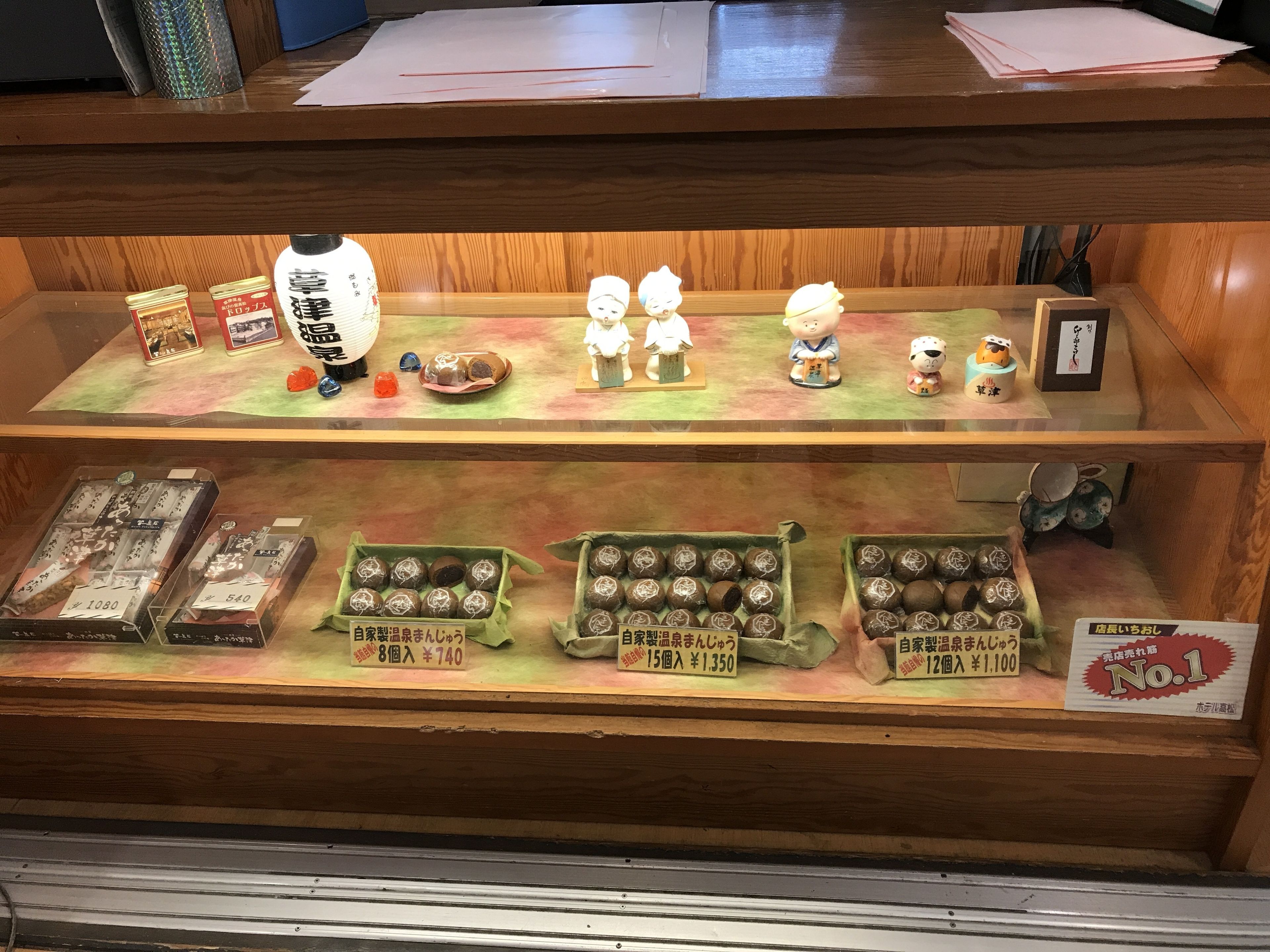 Une vitrine contenant divers objets, notamment des figurines, des produits emballés et des étiquettes de prix.