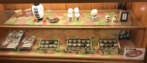 Une vitrine contenant divers objets, notamment des figurines, des produits emballés et des étiquettes de prix.