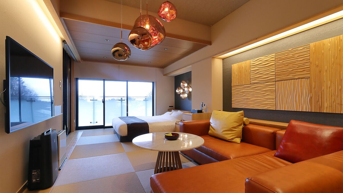 Una habitación de hotel moderna con un sofá, una mesita redonda, una cama y un ventanal grande.