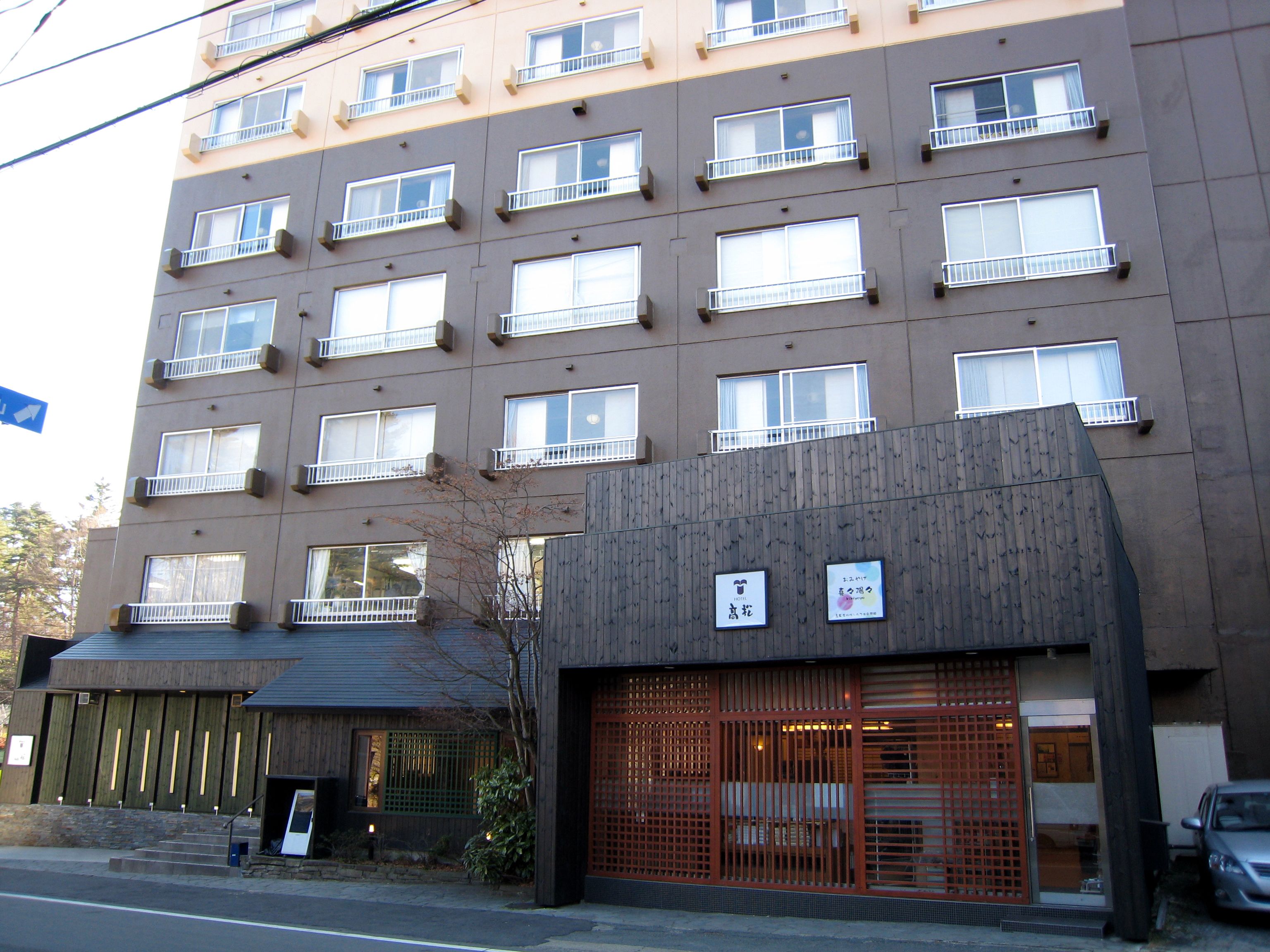 A multi-story hotel with a modern facade, multiple balconies, and a traditional entrance with a wooden gate.