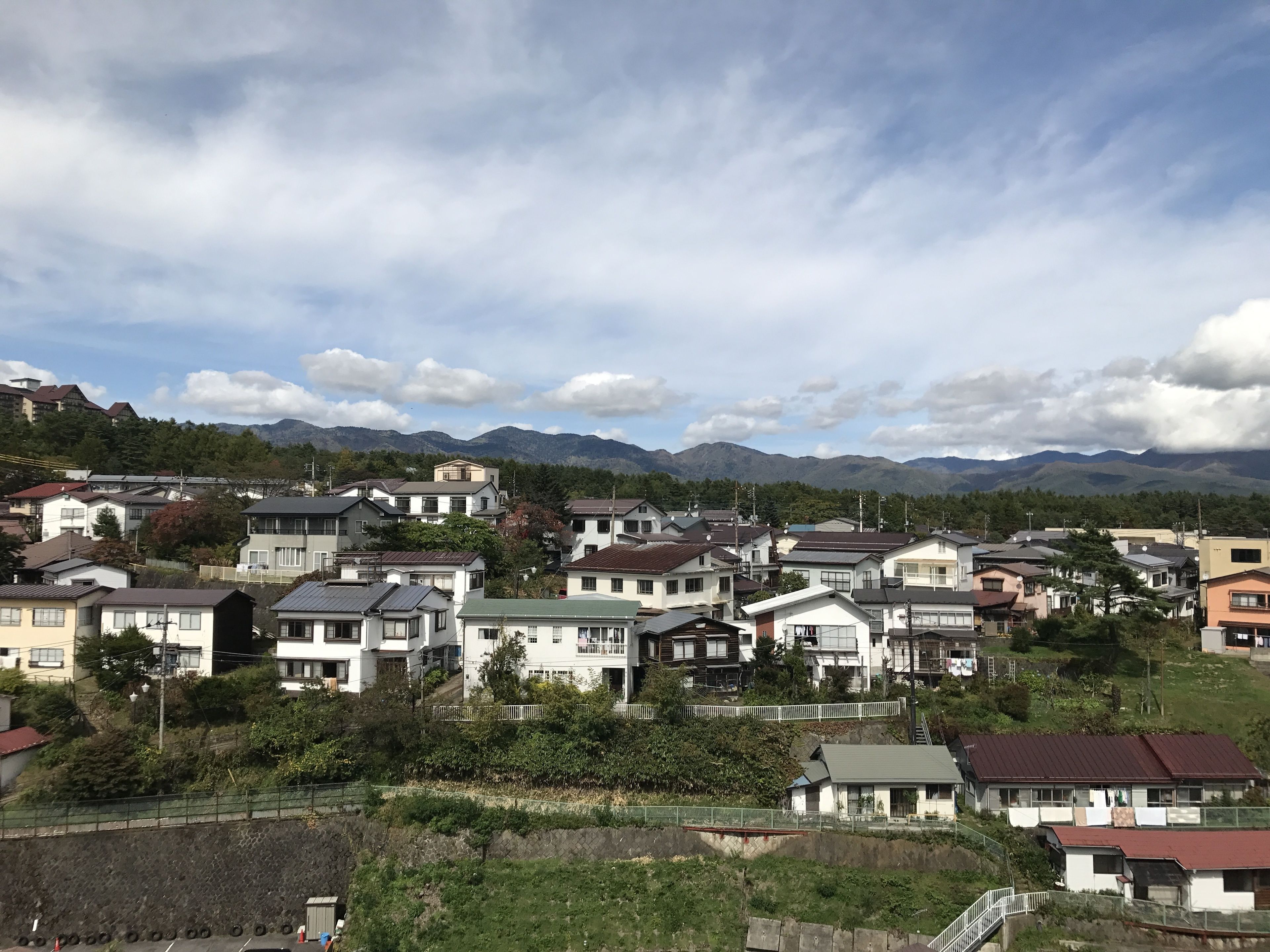 Zona residencial con casas, algunas con balcones a la vista, con montañas y un cielo parcialmente nublado al fondo.