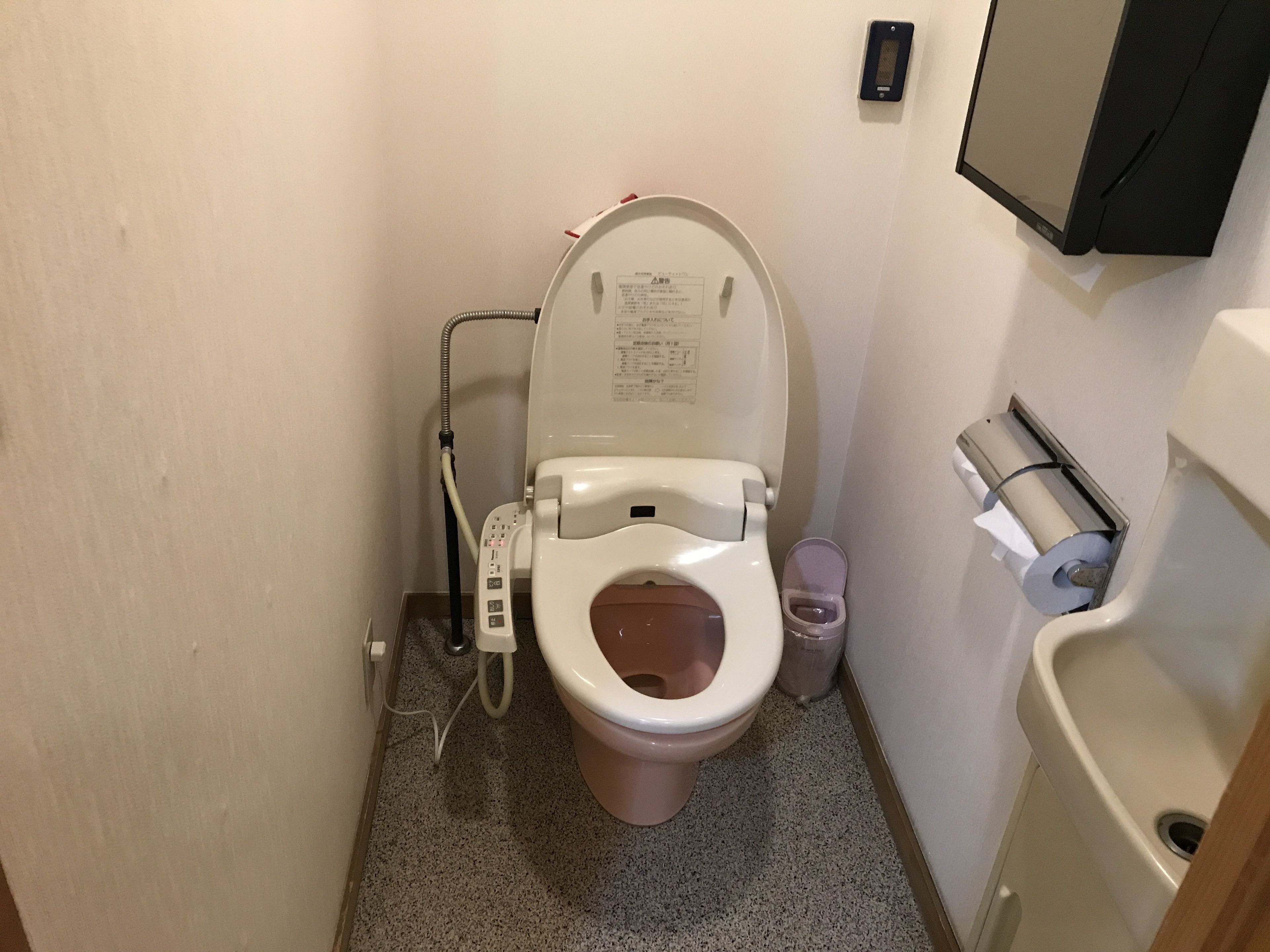A small bathroom with a toilet, a bidet, and a paper towel dispenser.