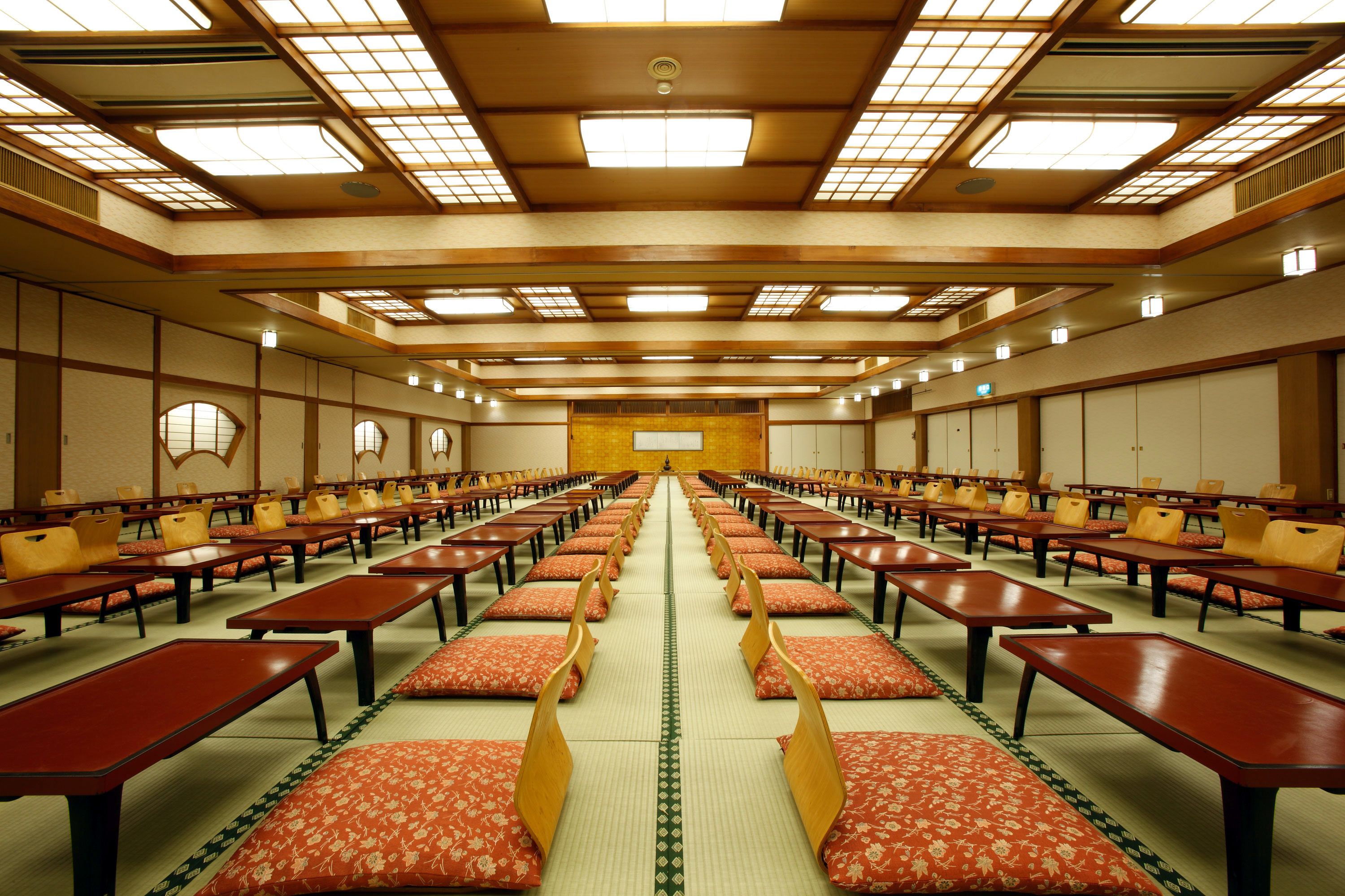 A conference room with rows of tables and chairs, a high ceiling with skylights, and a central projection screen.