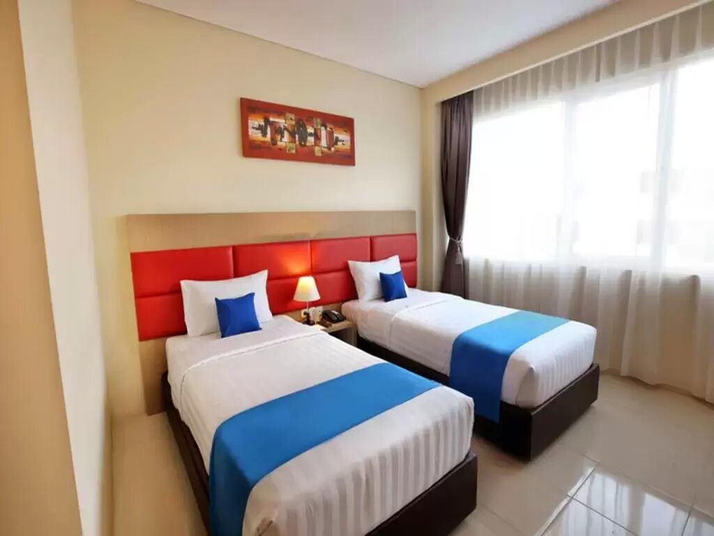 Ein Hotelzimmer mit zwei Betten, einem roten Kopfteil und einem Bild an der Wand.