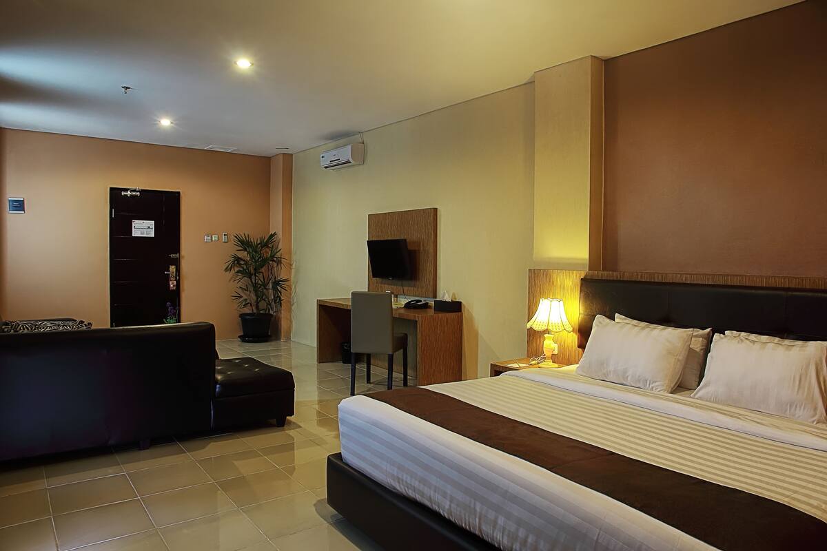 A hotel room with a large bed, a desk with a chair, a TV, and a potted plant.