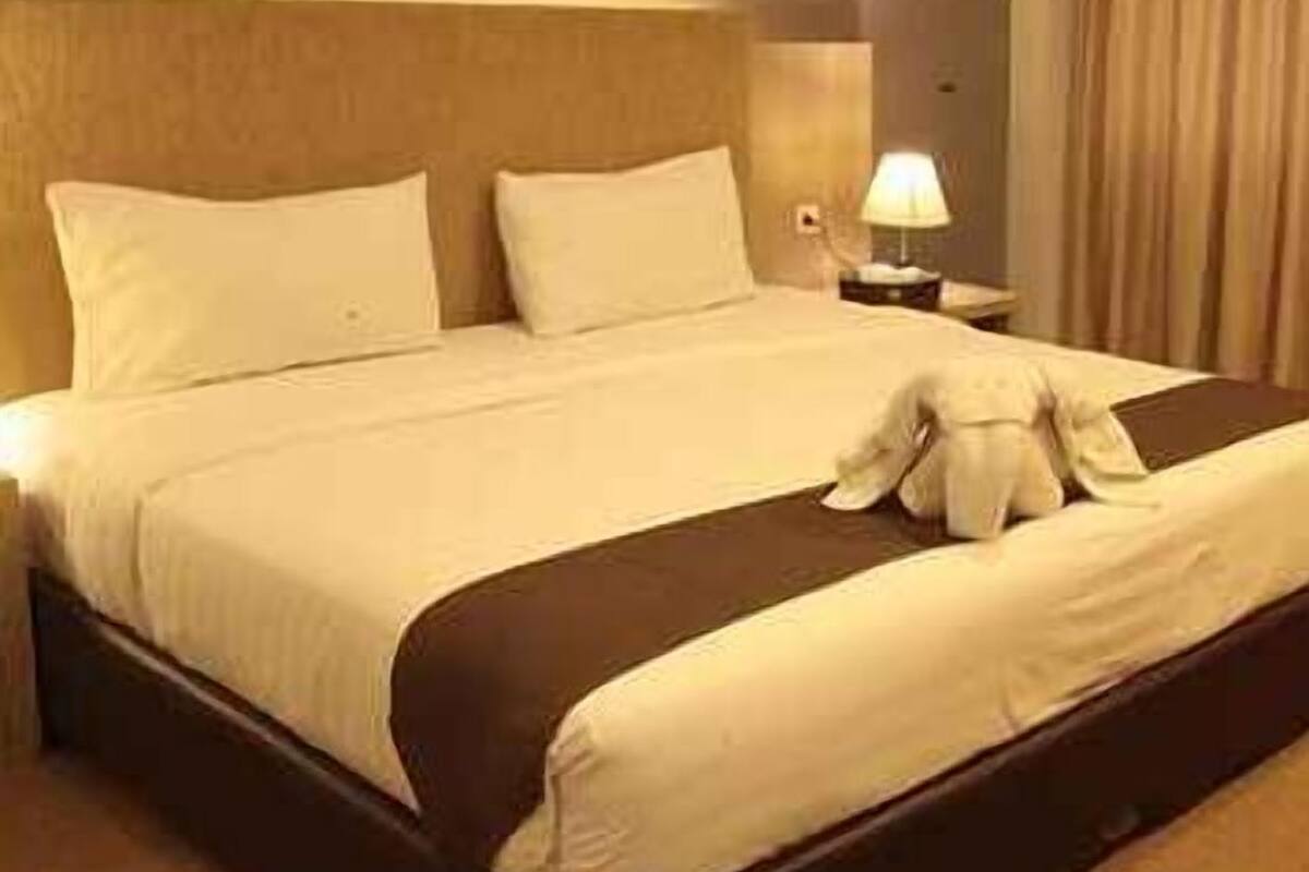 A hotel room with a large bed, a nightstand, a lamp, and a window with curtains.