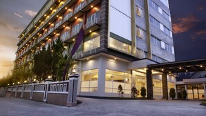 A multi-story hotel with a modern design, featuring balconies with railings, large windows, and a well-lit entrance area.
