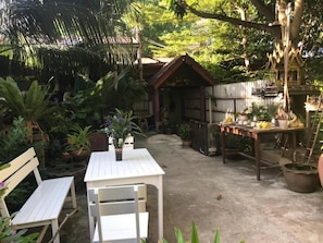 Eine rustikale Outdoor-Szene mit einem Holztisch und Bänken, umgeben von üppigem Grün und einer kleinen Holzkonstruktion.