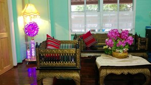 A traditional room with ornate furniture, a decorative lamp, and a window with a view of greenery. - Panida Suite (Bangkok)