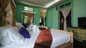 A hotel room with a large bed, a television, and a green wall. - Panida Suite (Bangkok)